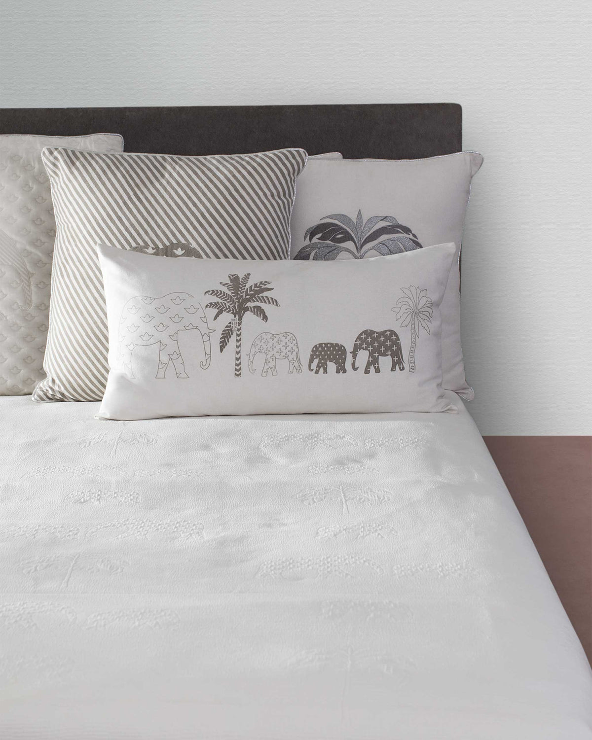 Ele Palm lumbar cushion cover placed on a bed among other cushions.