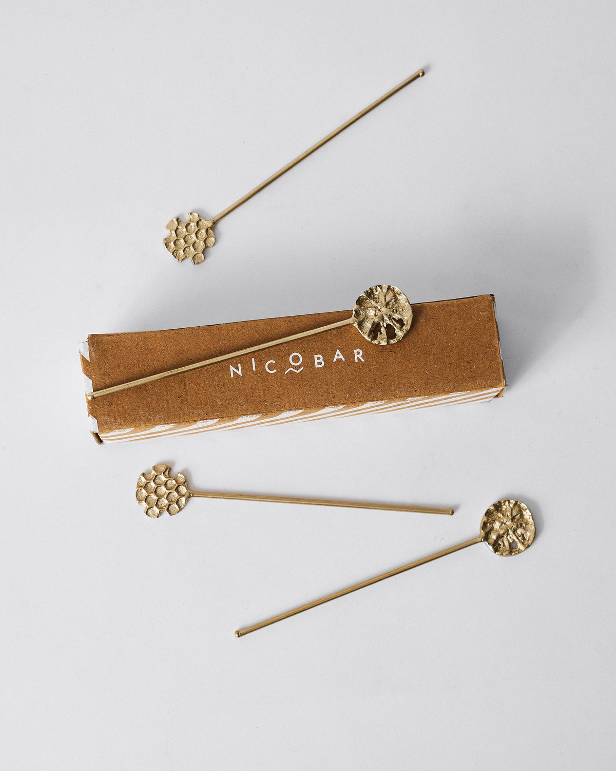 Gold Dawa stirrers arranged around their Nicobar gift box.