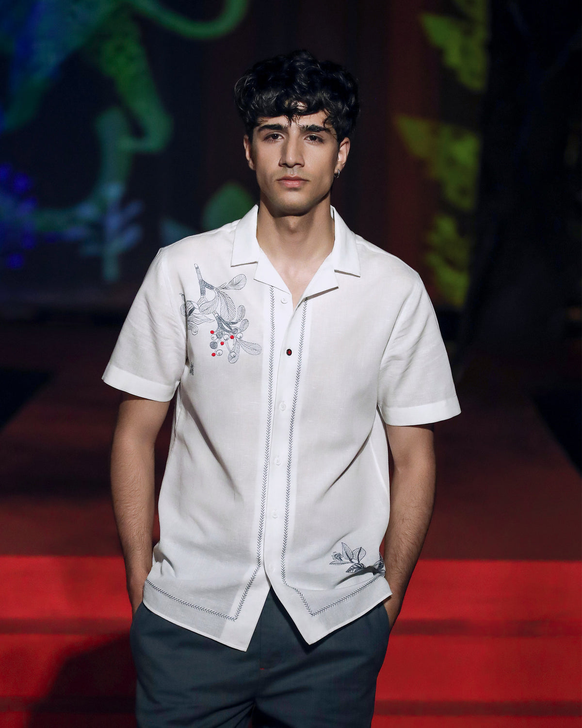 Person wearing a white Delta shirt with grey floral embroidery and red berries.