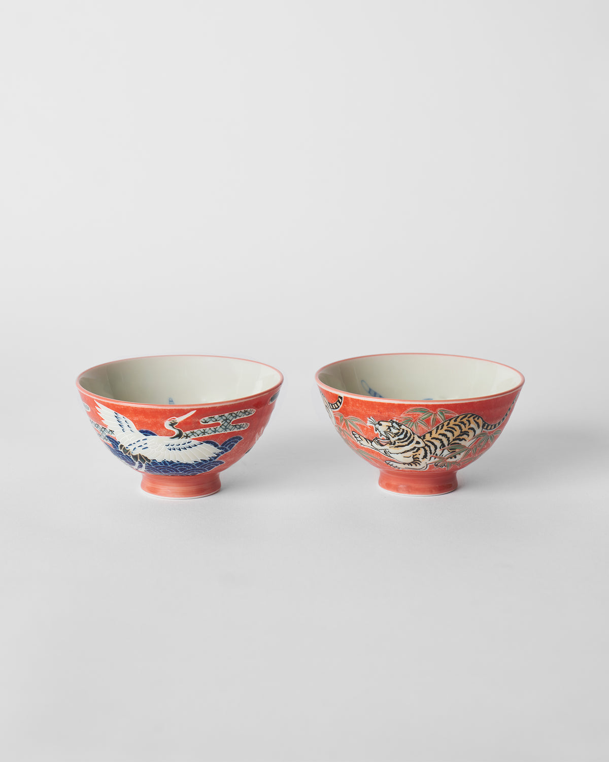 Front view of red Crane and Tiger bowls with crane and tiger illustrations.