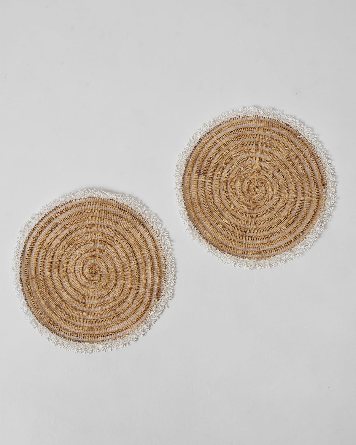 Pair of Kaveri Placemats with a round woven design and fringed edges.