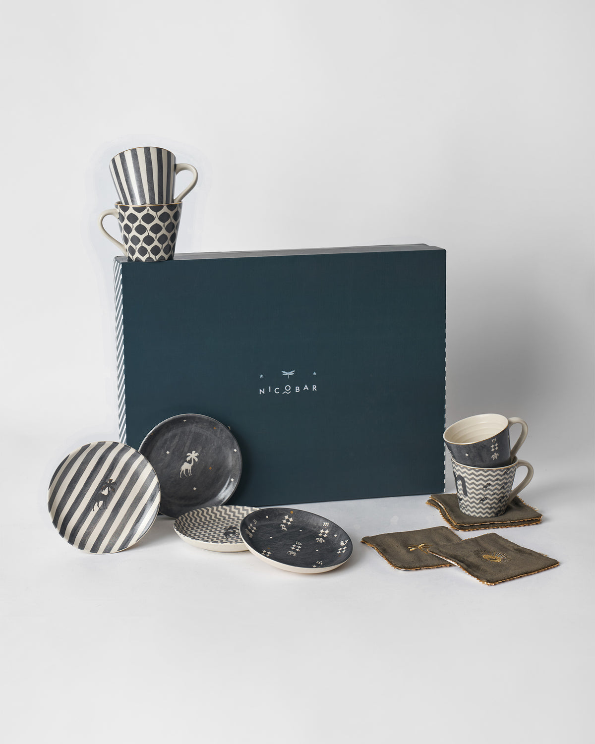 Twilight gift set of charcoal mugs, plates and olive coasters around a teal Nicobar box.