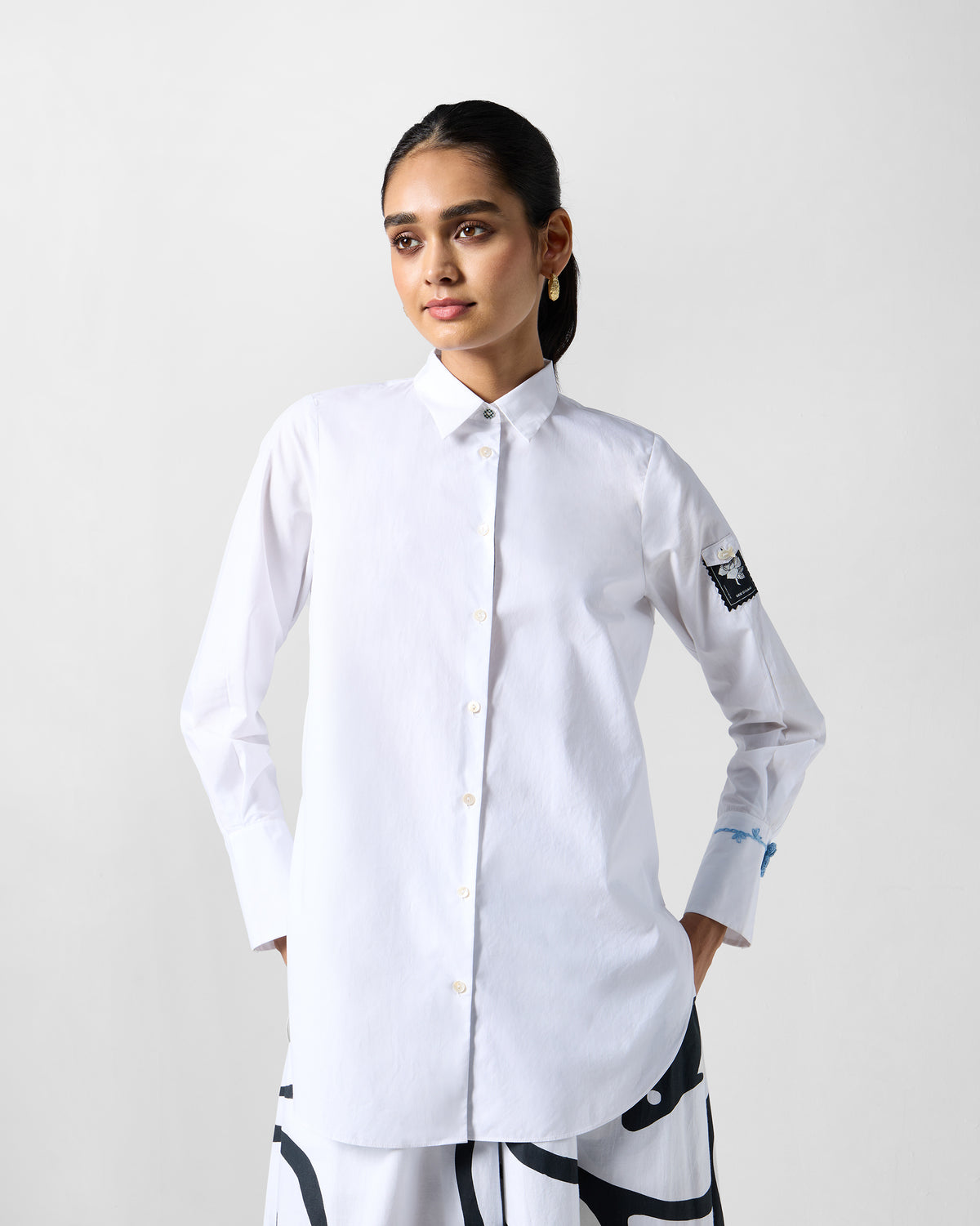 Person wearing a white trench shirt with a gulaab stamp patch on the sleeve.