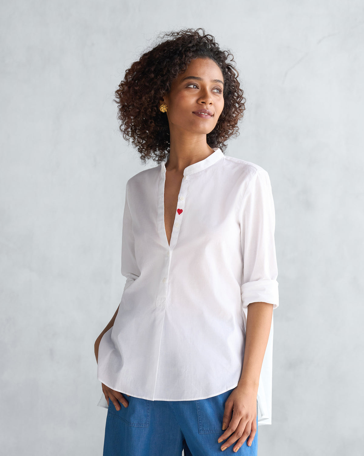 Person wearing a white mandarin collar top with a red heart.