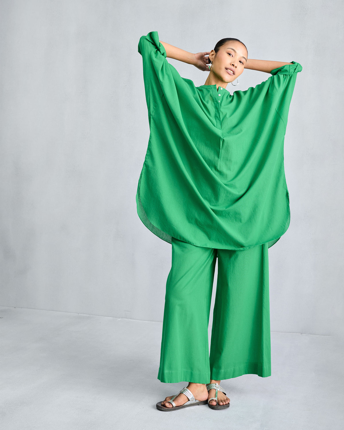 Person with both arms lifted, showing the loose drape of a green Lazy Sunday Tunic.
