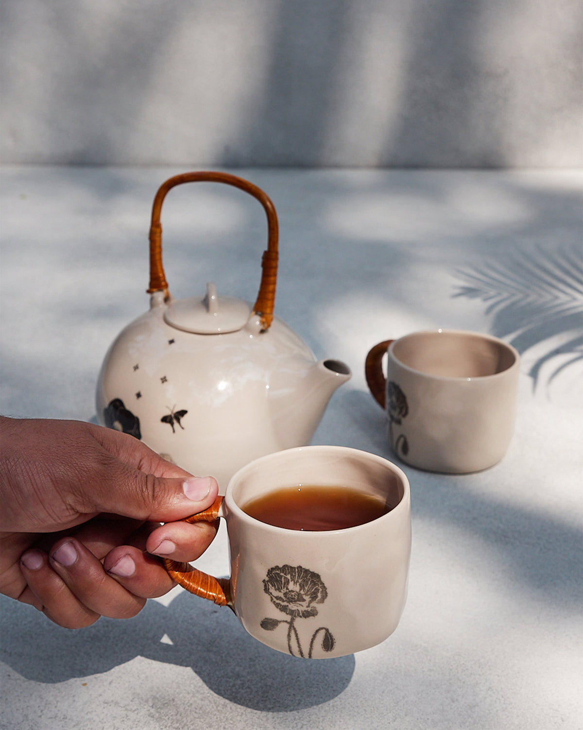 Poppy mug with a rattan handle held with tea beside a teapot.