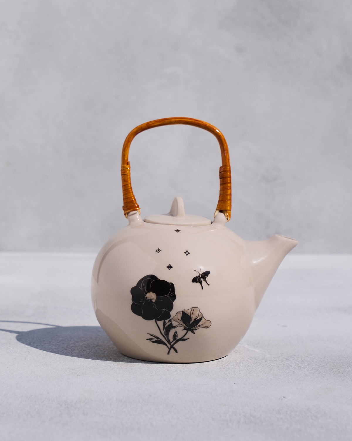 Ivory Poppy teapot with rattan handle and black poppy illustrations.