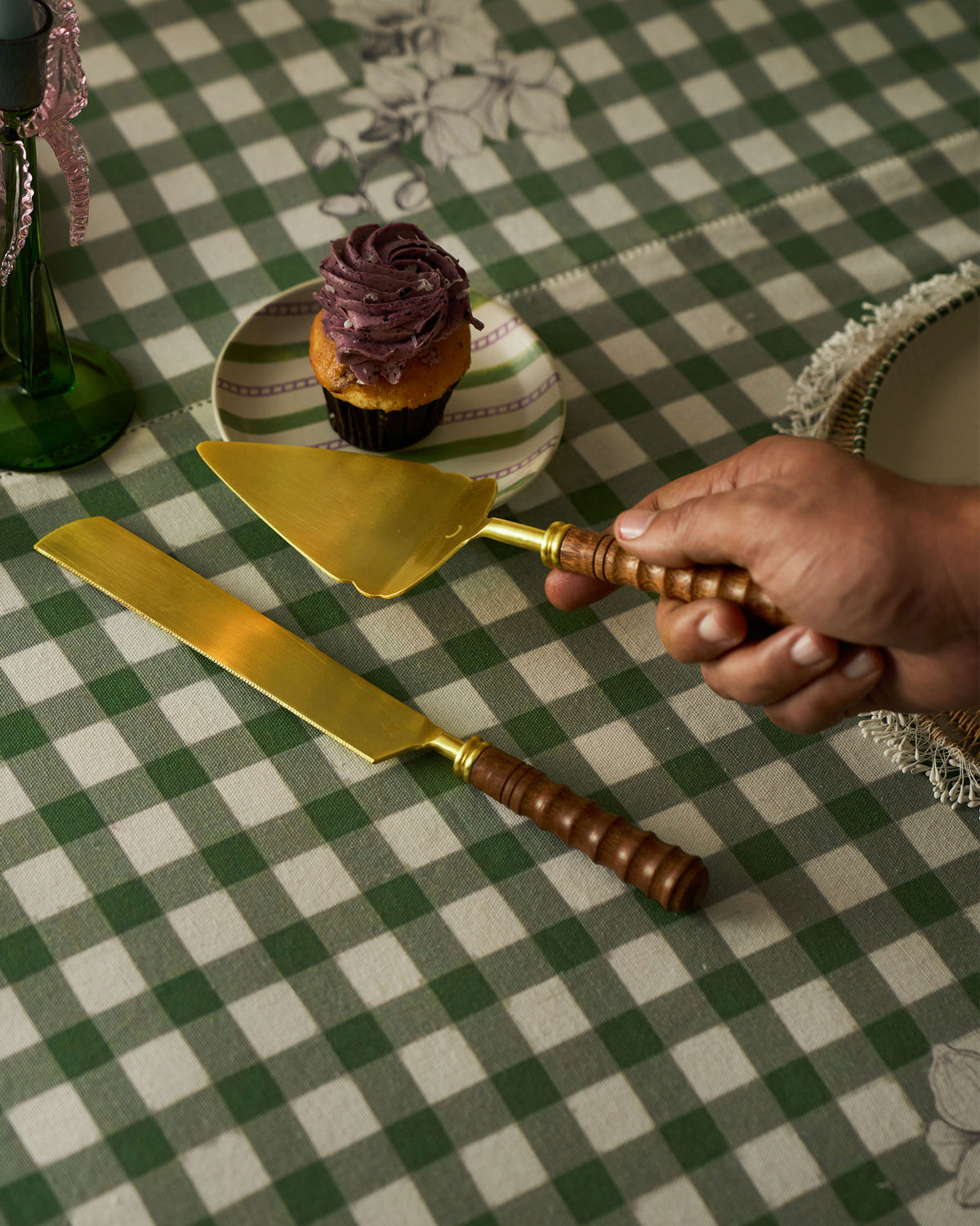 Hand holding a gold cake server with a ribbed wood handle.