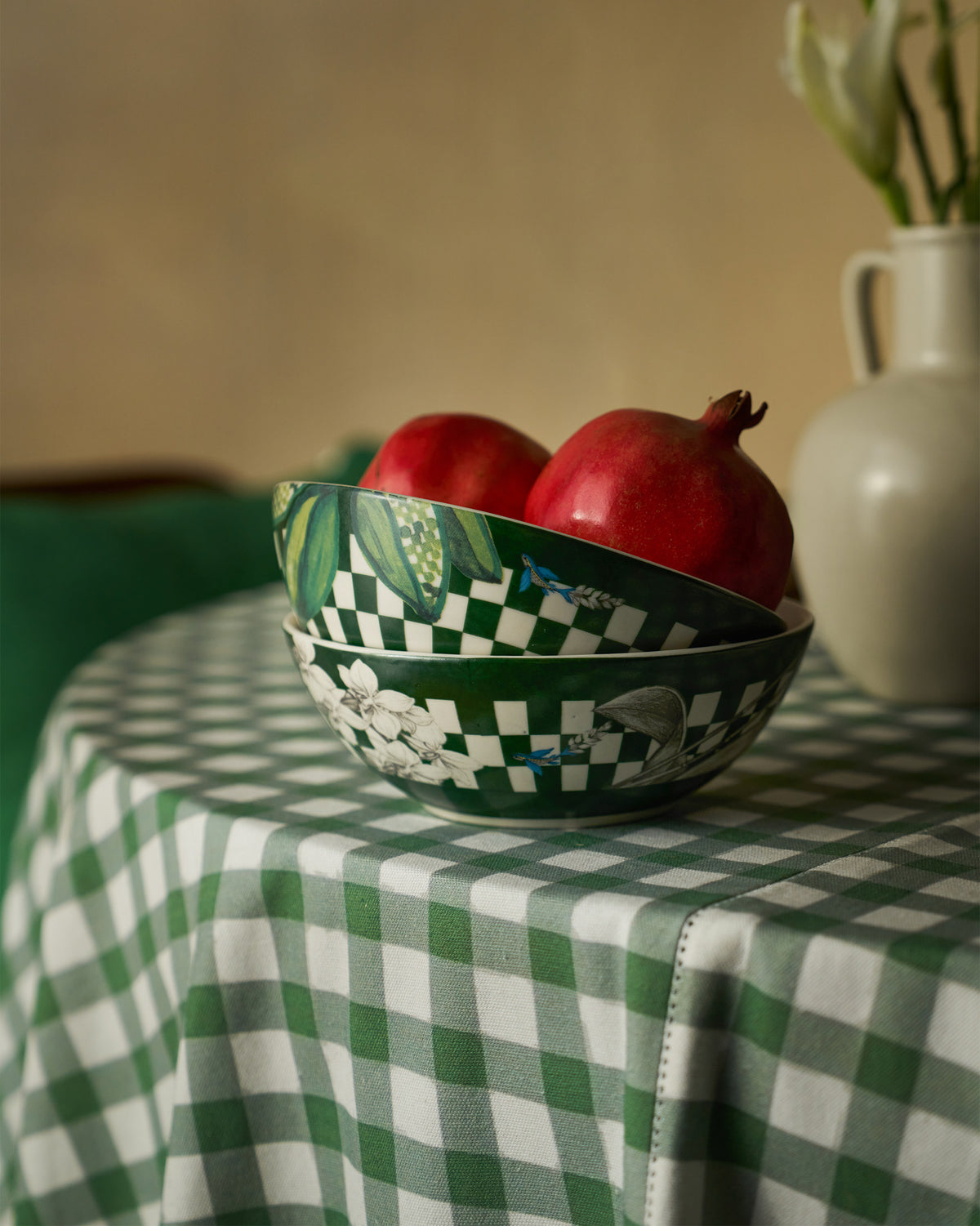 Stacked green Reesha bowls holding pomegranates on a checkered tablecloth.