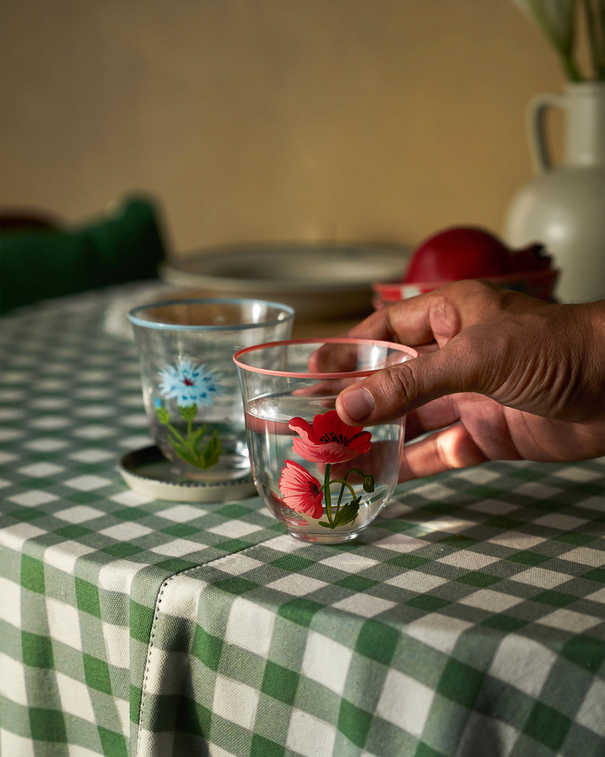 Rit tumbler with a red poppy motif being lifted from a green checkered table.