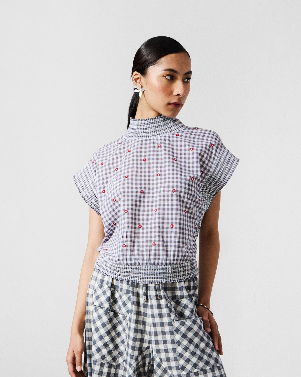 Person wearing the Lehar top in grey gingham with red embroidered dots and a smocked waistband.
