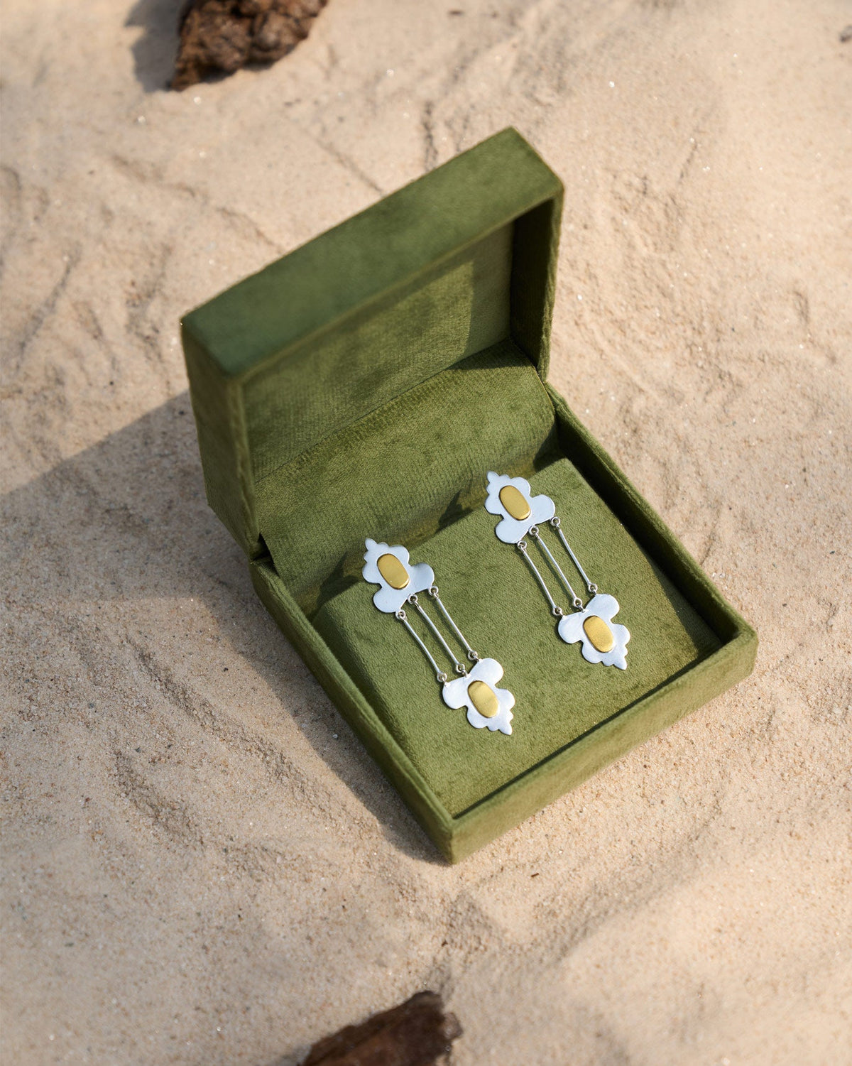 Pair of Champa Drop Earrings in a green velvet box on sand.
