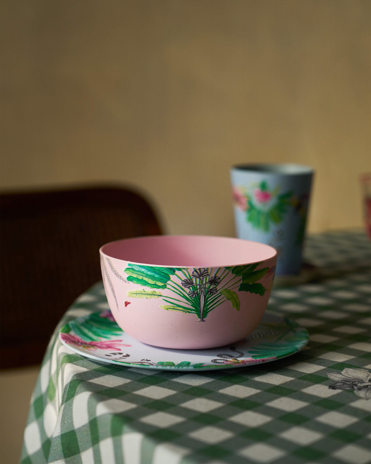 Pink Toucan bamboo cereal bowl on a tropical plate with a matching blue tumbler behind.
