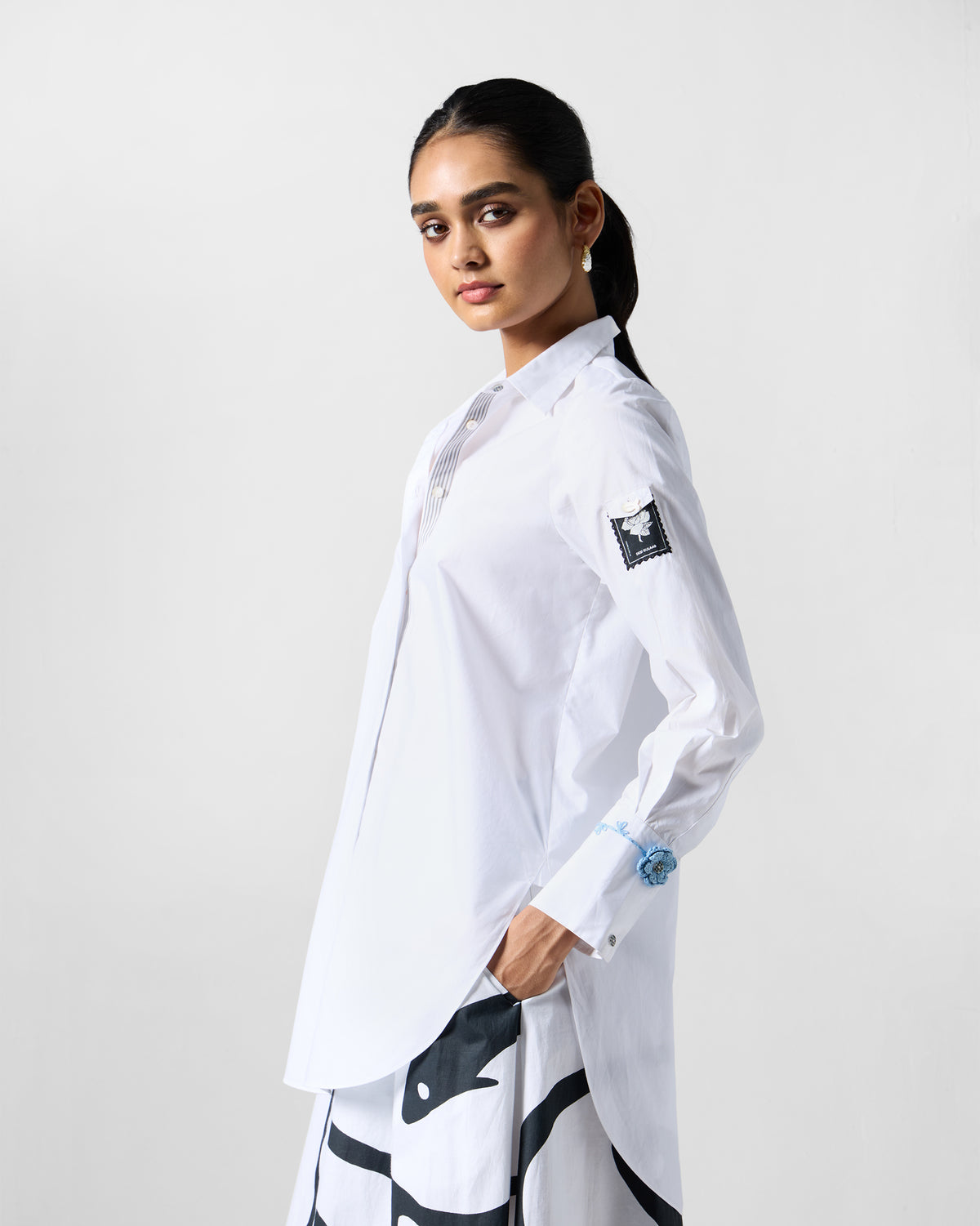 Side view of a white trench shirt with a sleeve patch and blue cuff flower.