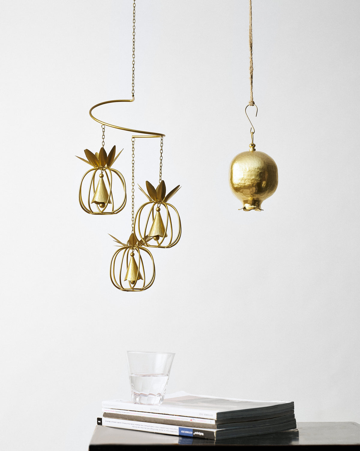Gold pineapple wind chime and Anar pomegranate bell hanging on a wall.
