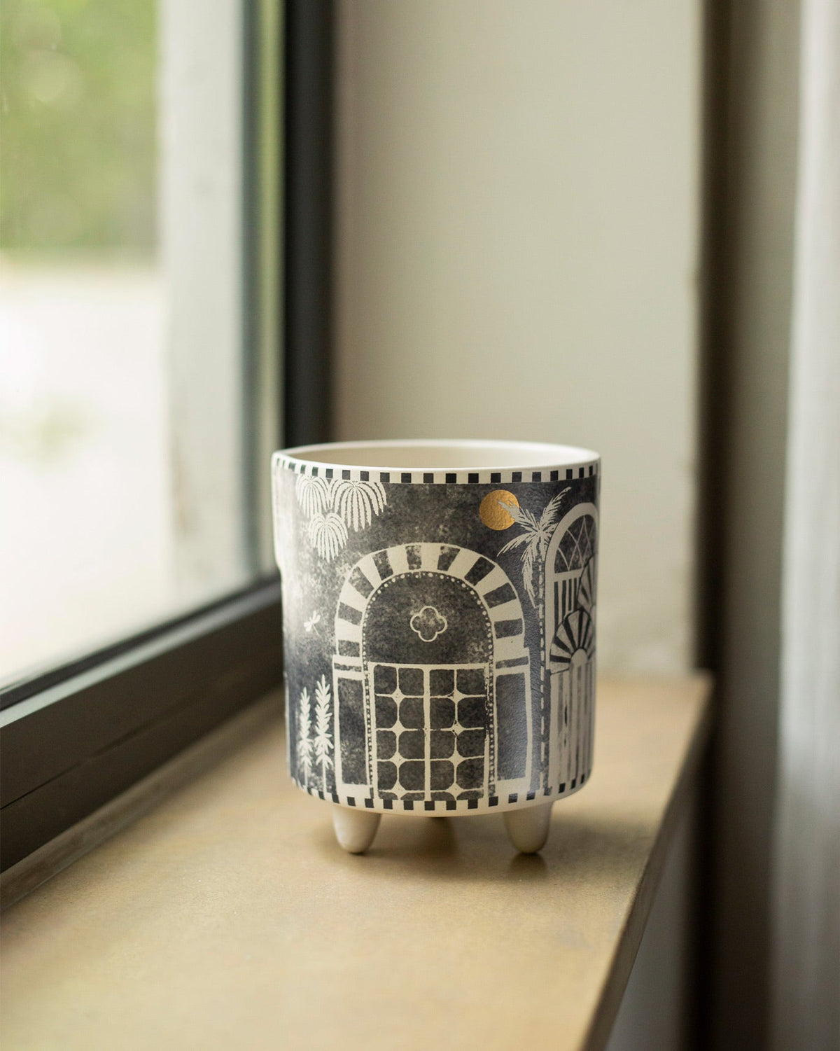 Monochrome planter with arch and palm print on a windowsill.