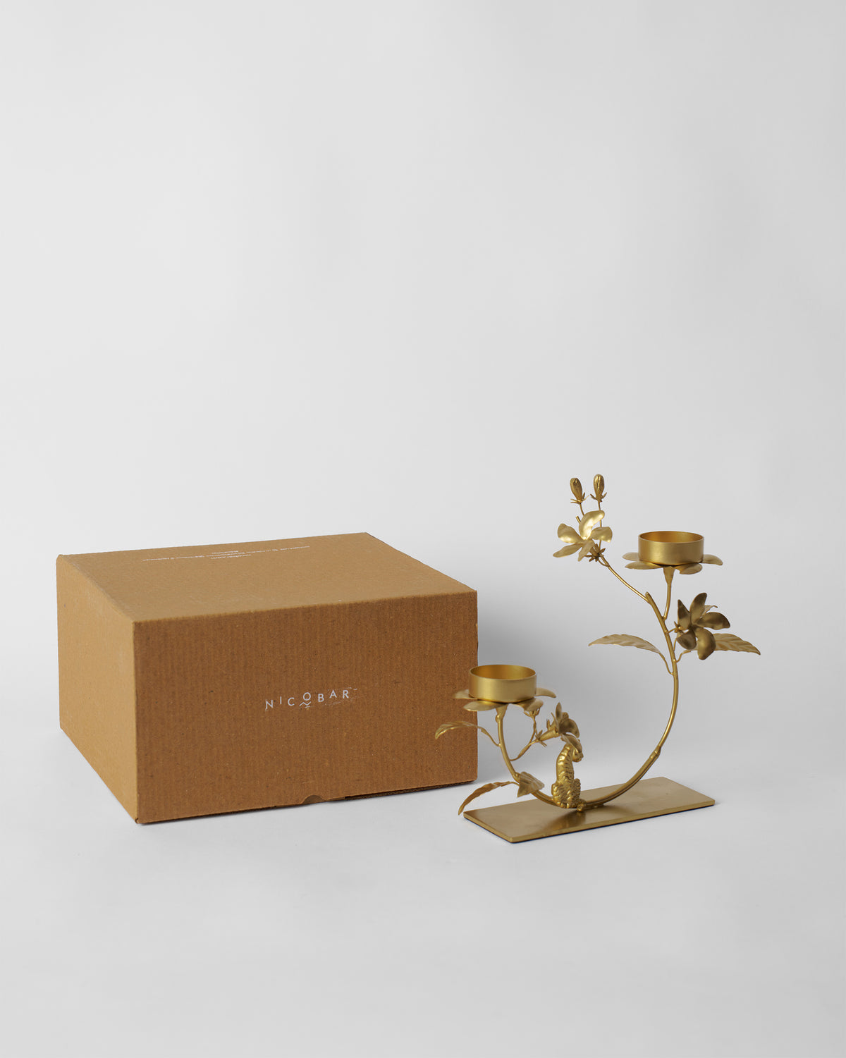 Jasmine Bloom Tealight Holder in gold beside a kraft Nicobar gift box.