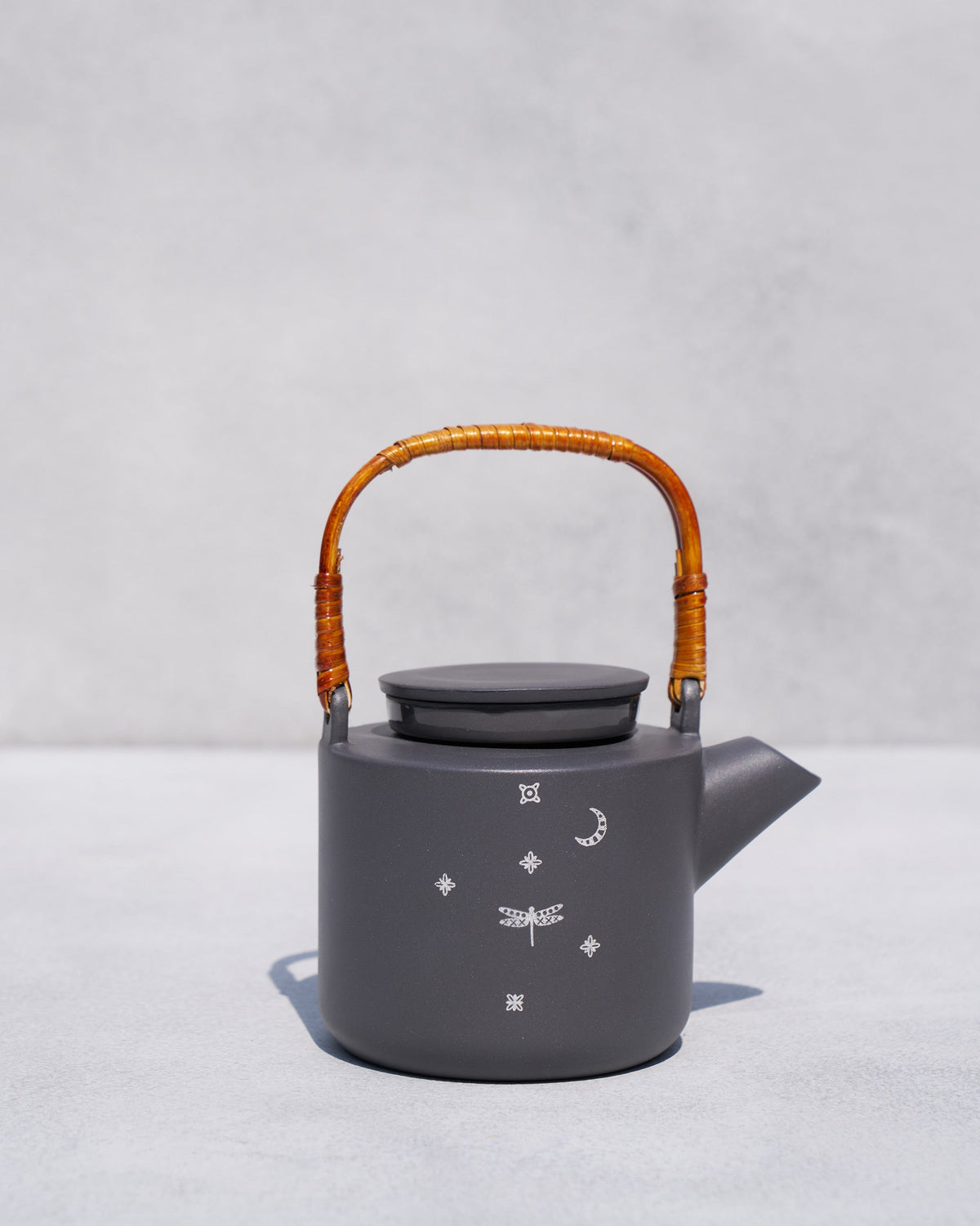 Matte charcoal Taramandal teapot with a rattan handle and white celestial motifs.