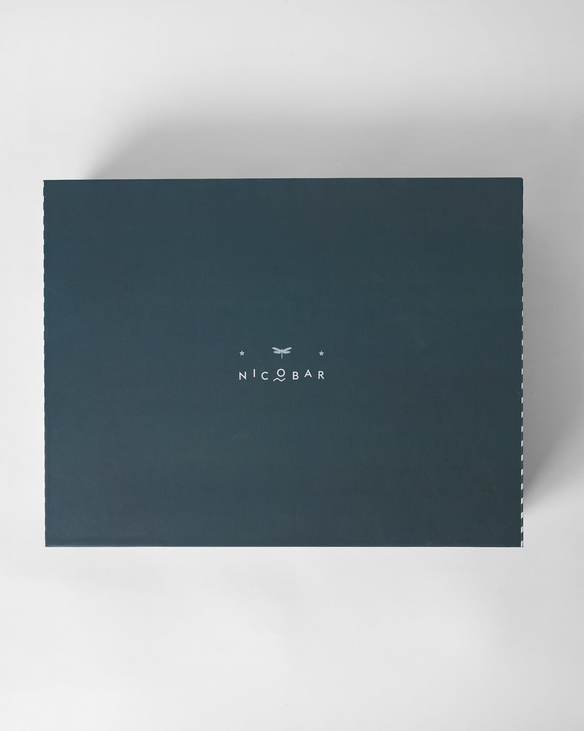 Closed dark teal Nicobar gift box for the Twilight set with a dragonfly logo.