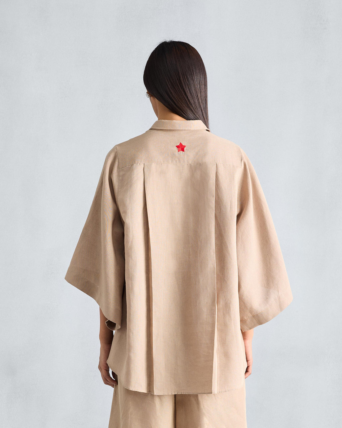 Back of a beige Drop Armhole shirt with yoke pleats and a red embroidered star.