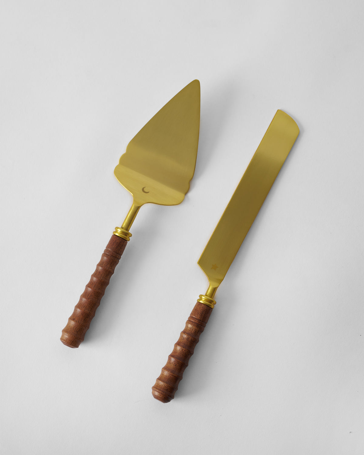 Gold cake knife and server laid diagonally on a plain surface.