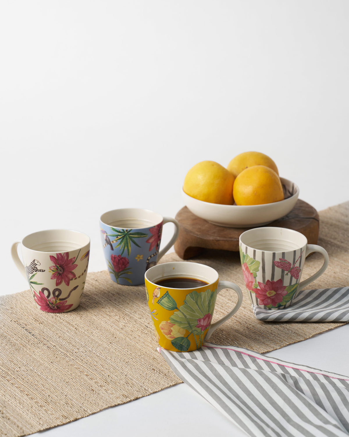 Wilderness mugs on a jute runner, including a mustard lotus mug filled with coffee.