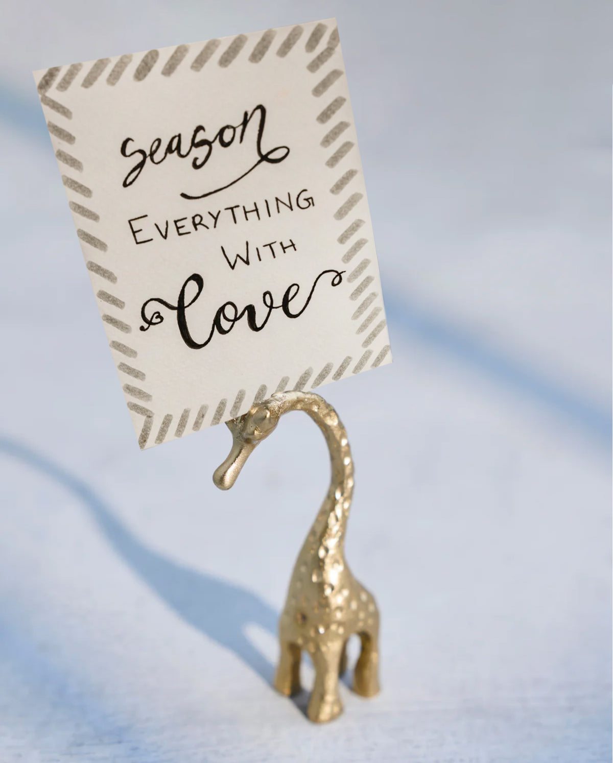 Giraffe Menu Card Holder in brass holding a printed card with a handwritten message.