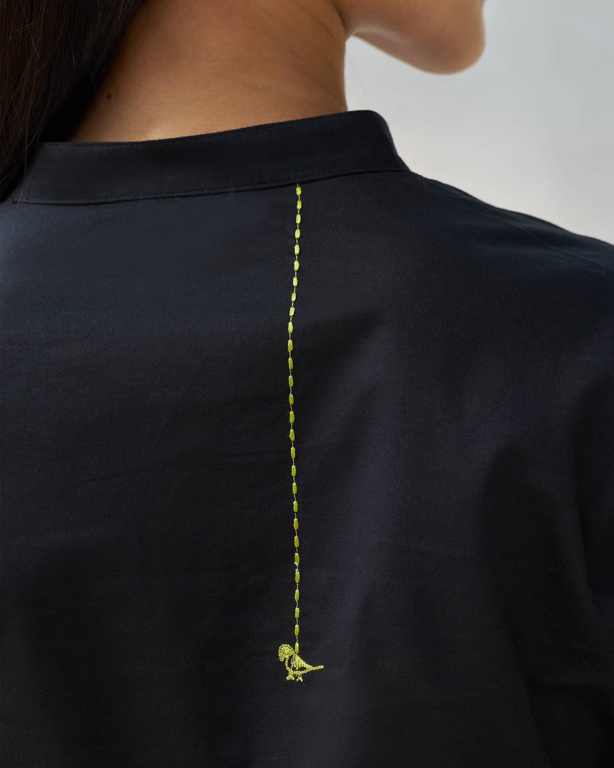 Close-up of a green embroidered bird on the back of a black kurta.