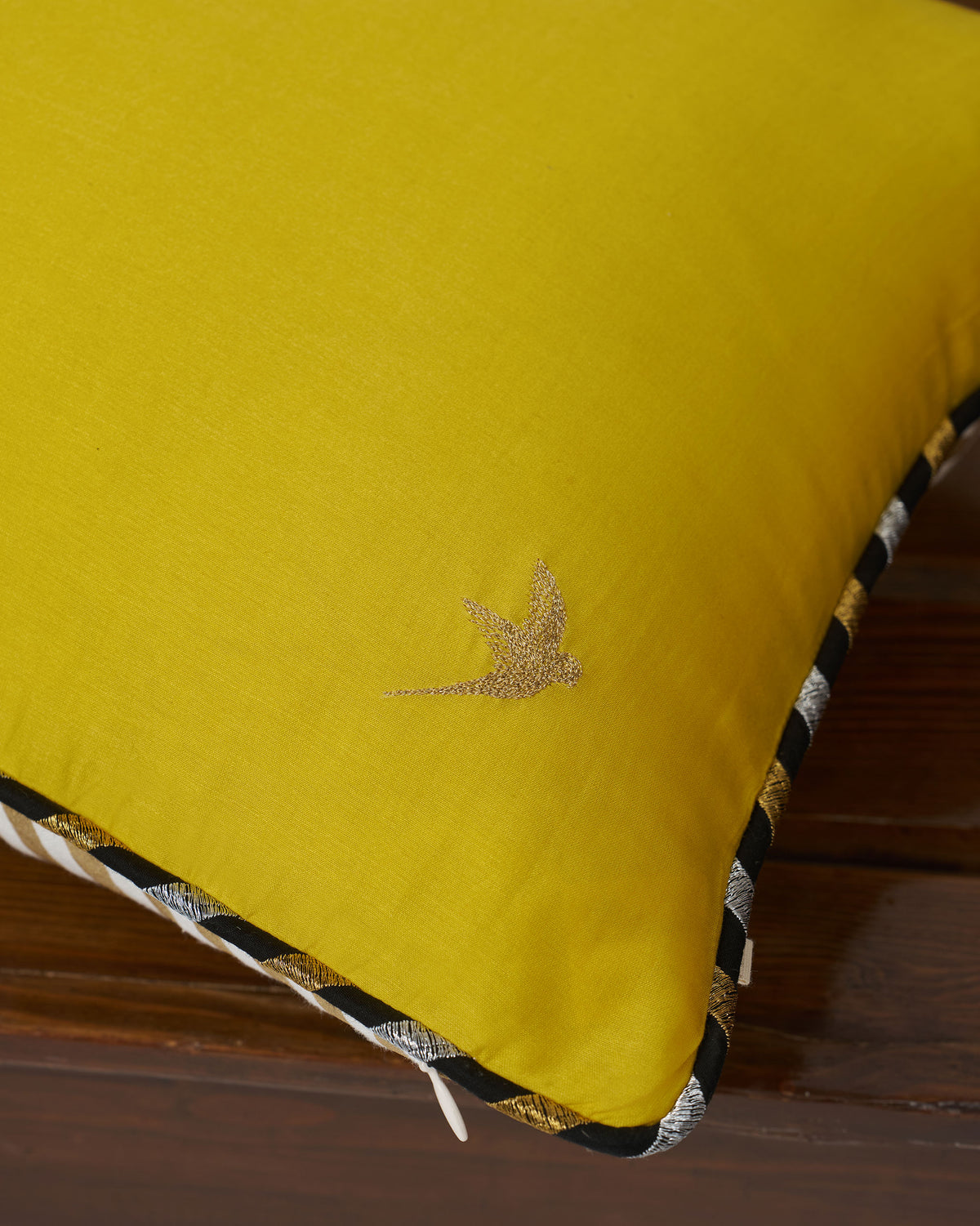 Close-up of a Midas cushion cover corner showing a gold bird embroidery.