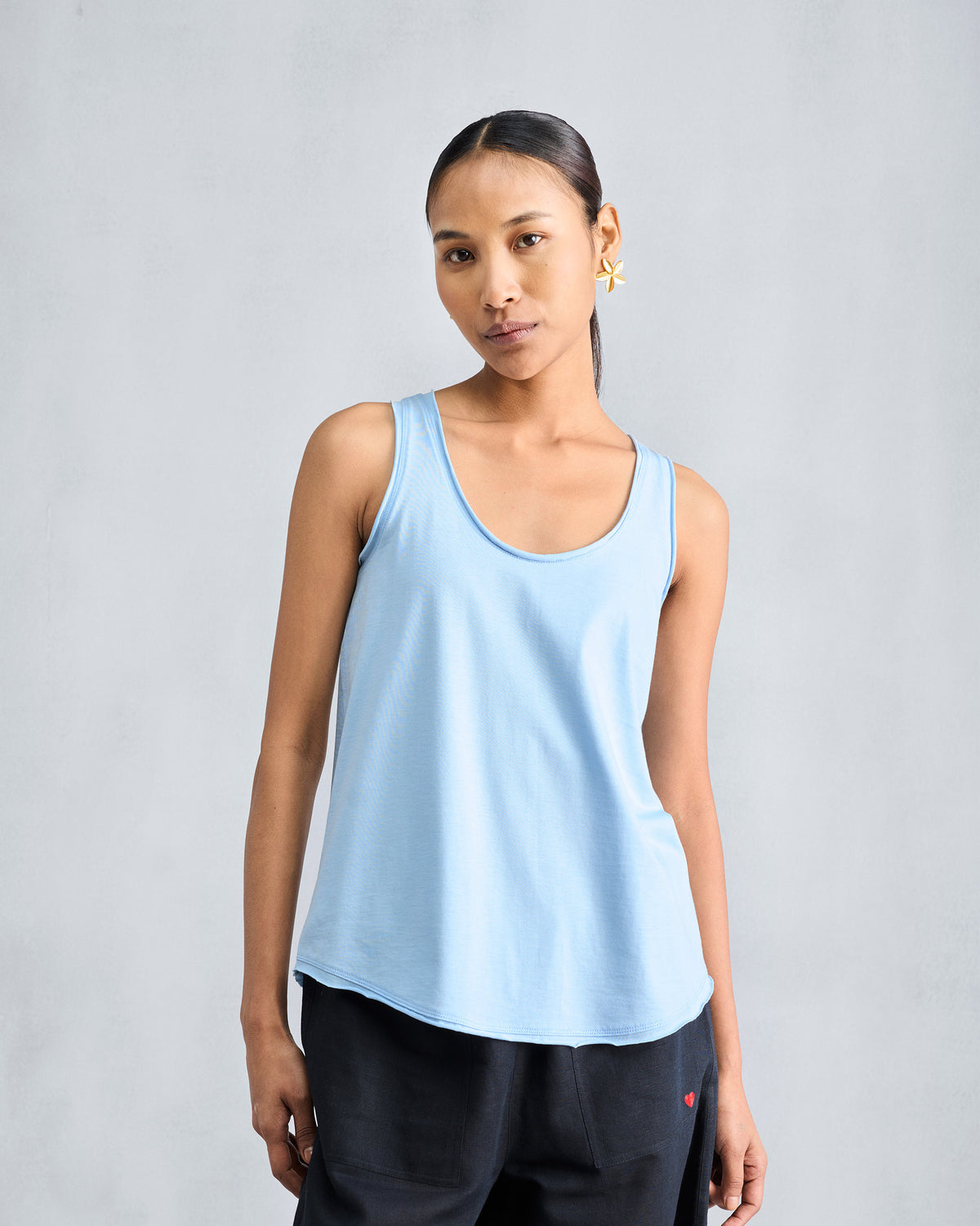 Person wearing a light blue tank with a scoop neck and curved hem.