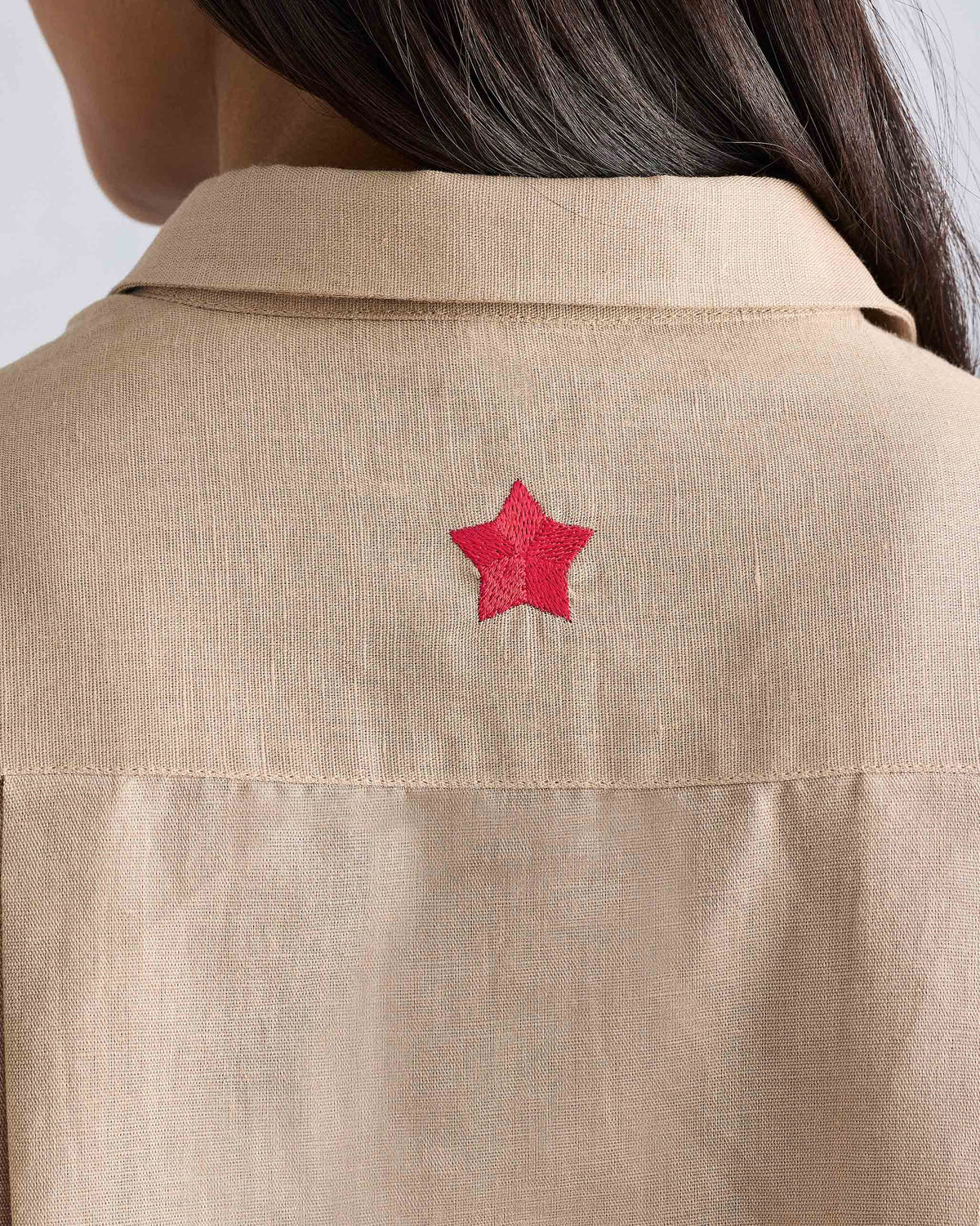 Close-up of a red embroidered star on the back of a beige Drop Armhole shirt.