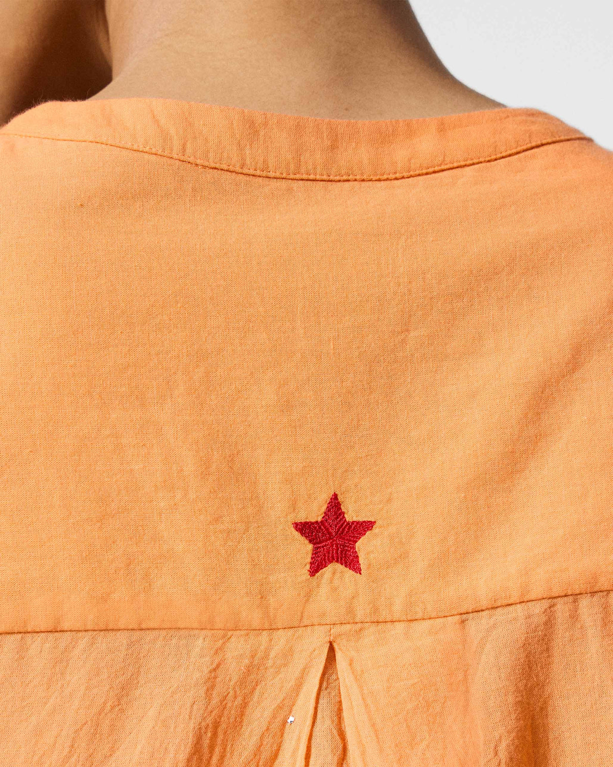Close-up of a red embroidered star on the back of an orange Lazy Sunday tunic.