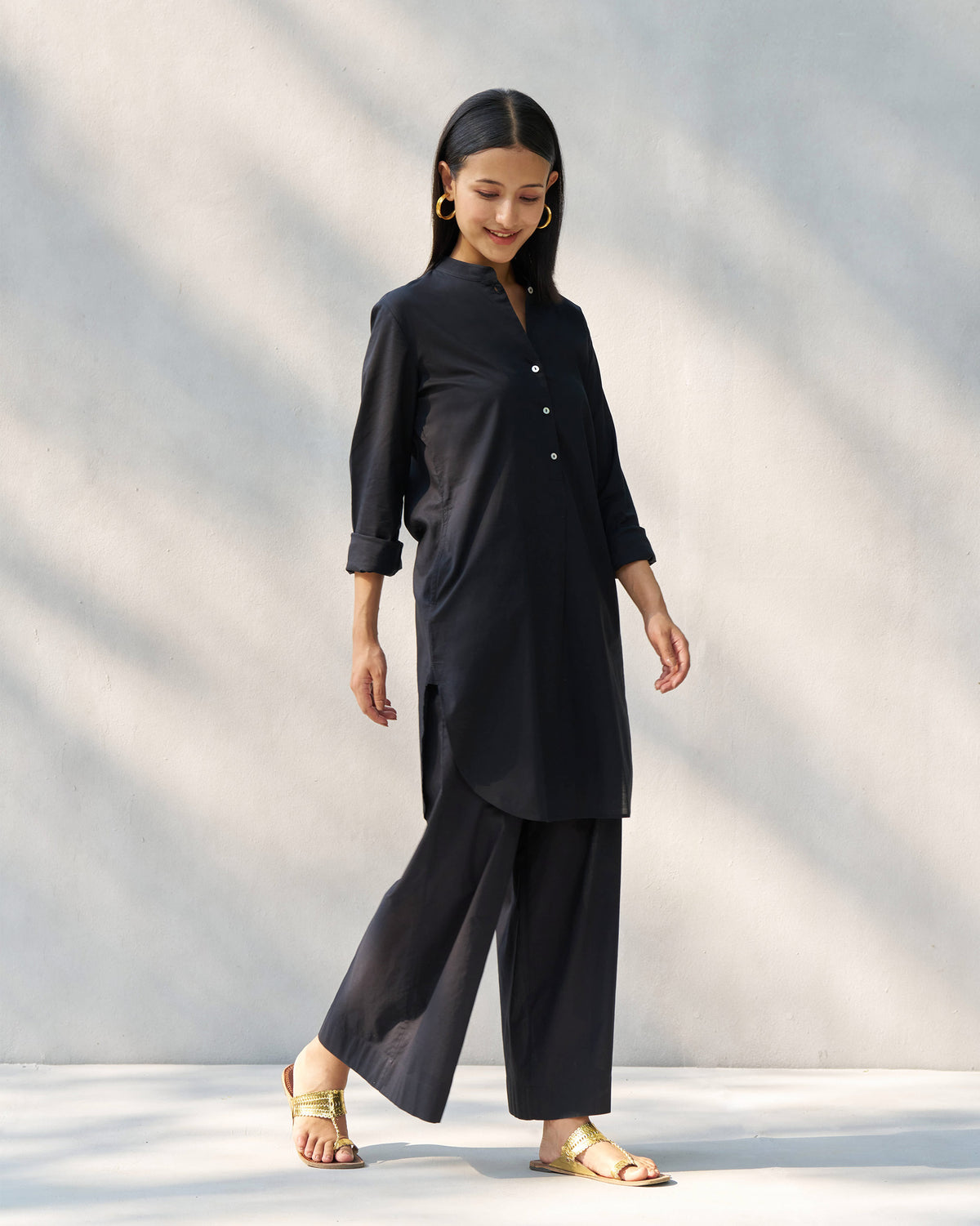 Person wearing a black Stone set tunic with a curved hem and wide pants.