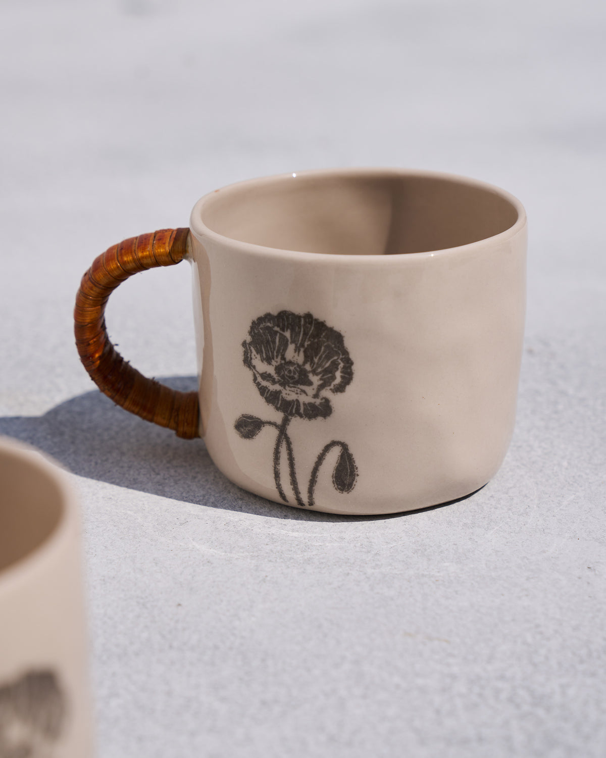 Close-up of a Poppy mug with a black poppy print and rattan handle.