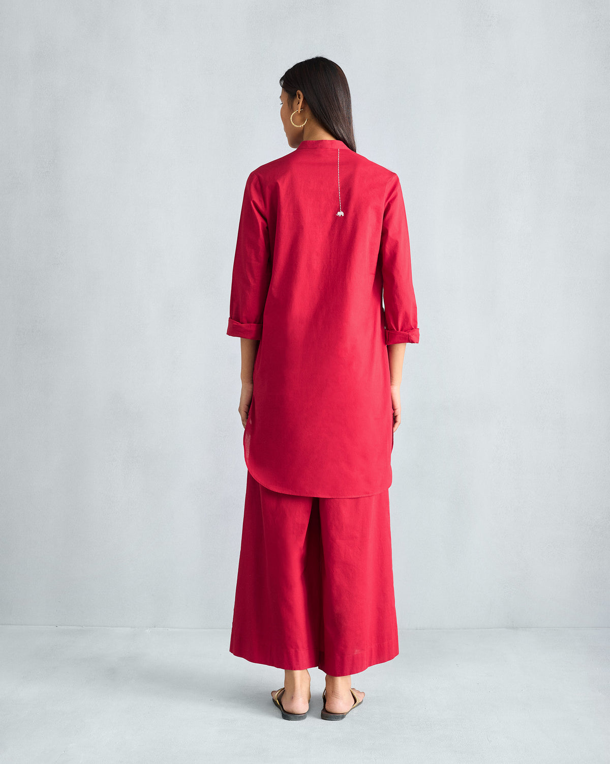 Back of a red mid-length kurta set with a curved hem and matching trousers.