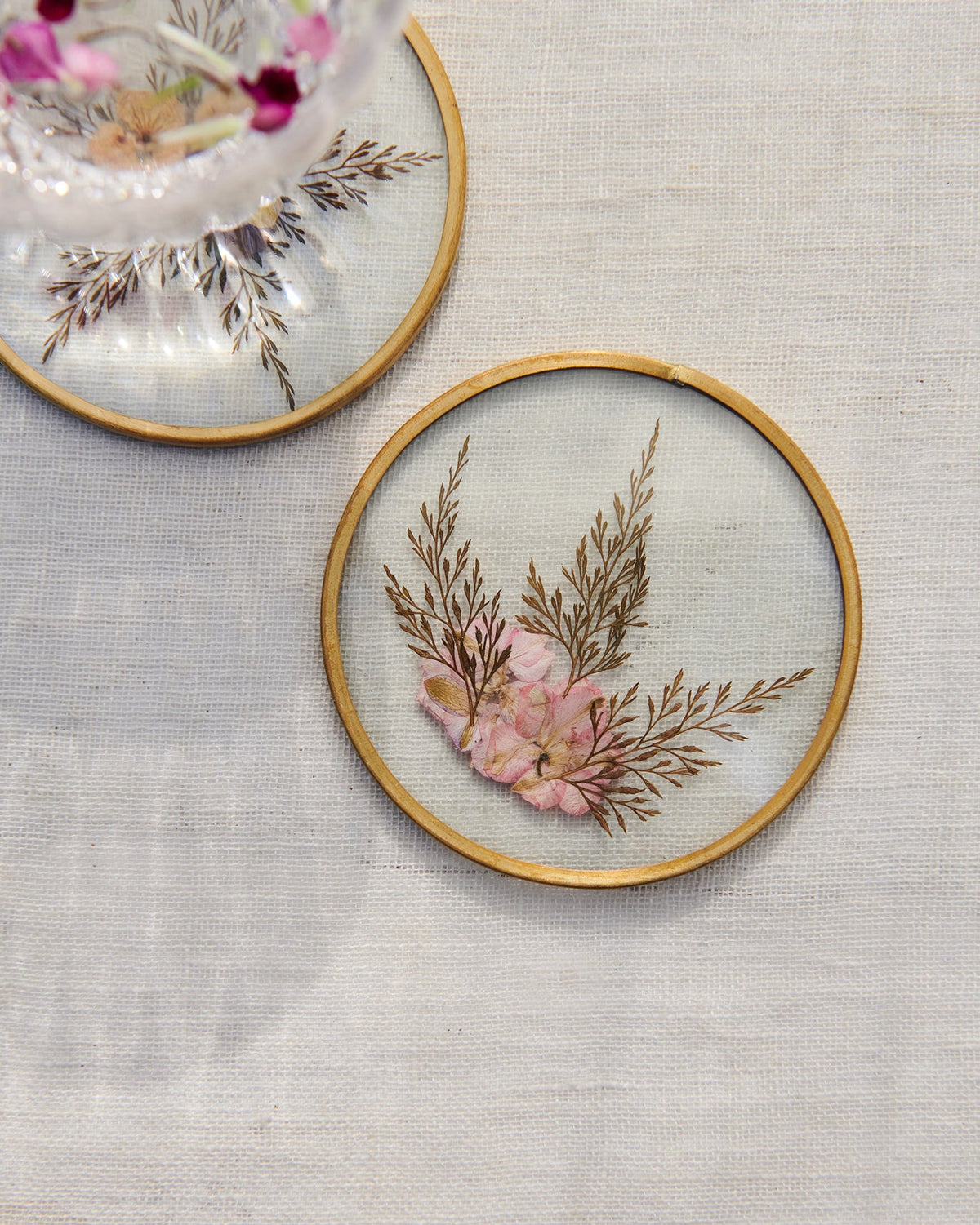 Close-up of a Palm Grove glass coaster with pink pressed flowers and ferns.