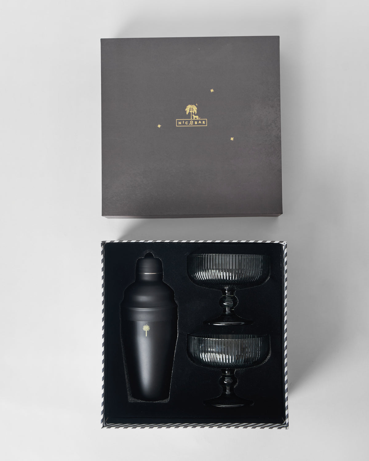 Open Avi bar gift box with black shaker and stacked smoked coupe glasses.