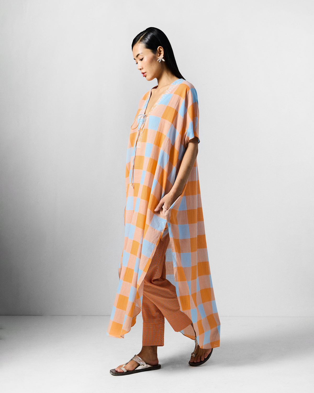 Person wearing an orange and blue check Vaya kaftan with a side pocket.