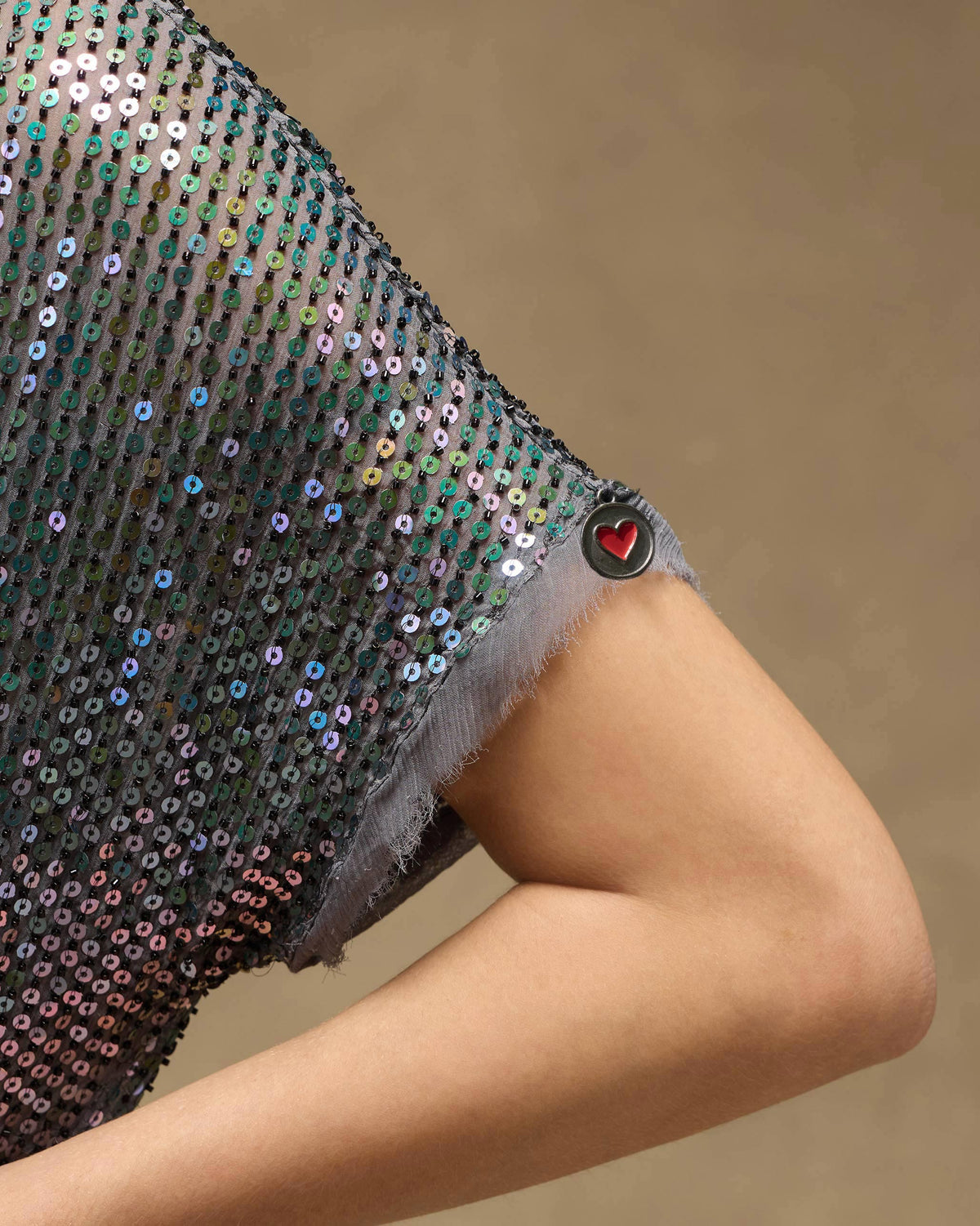 Close-up of a sequined Shimmer dress sleeve with a red heart charm.