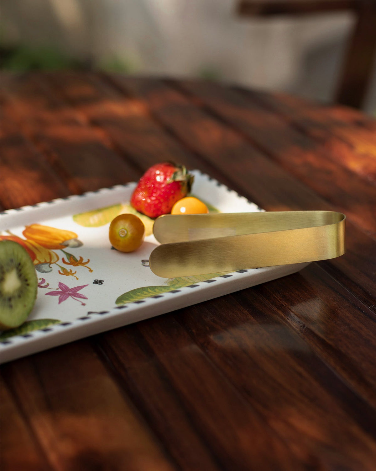 Brass tongs resting on the Mahi cookie tray with cashew fruit print.