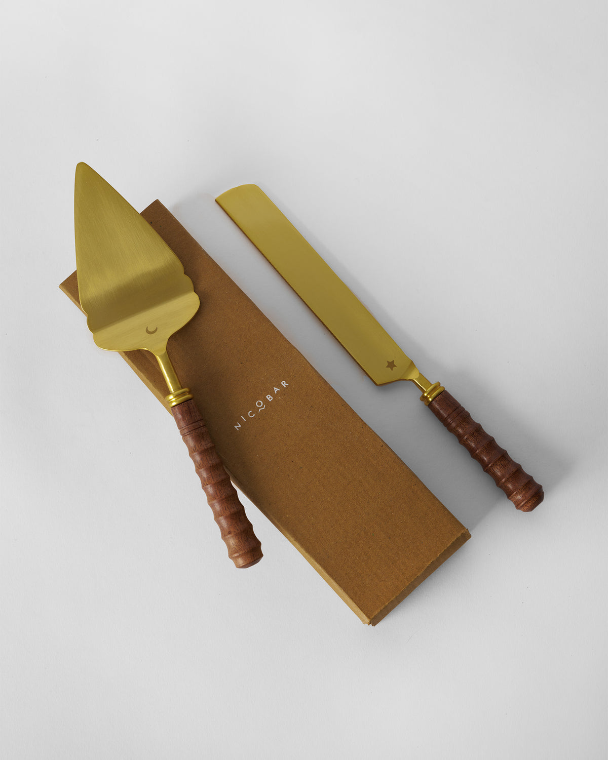 Gold cake knife and server resting on a Nicobar gift box.