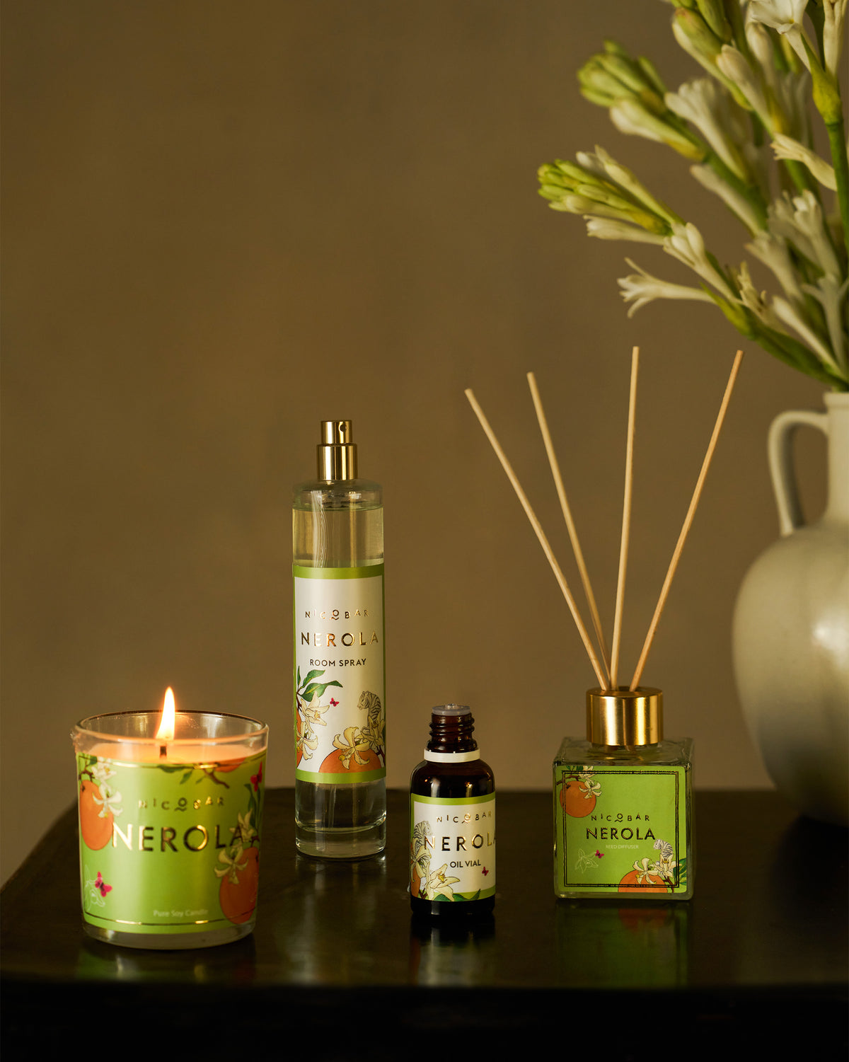 Lit Nerola candle with room spray, oil vial, and reed diffuser on a table.