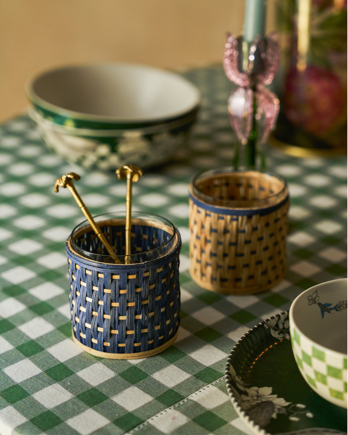 Bloom rattan condiment jars styled with ceramic bowls on a gingham tablecloth.