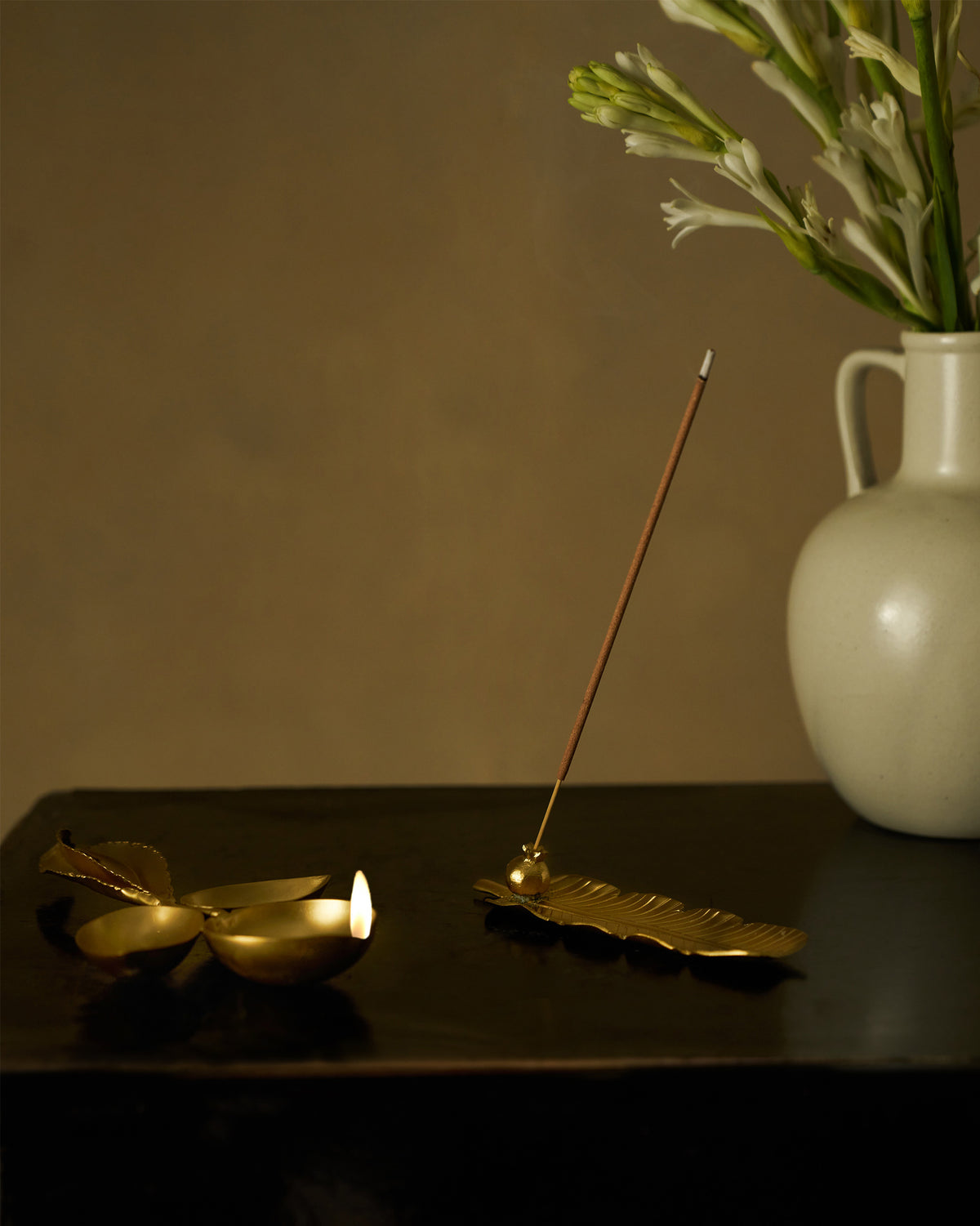 Lit Taal brass diya and leaf incense holder on a dark table.