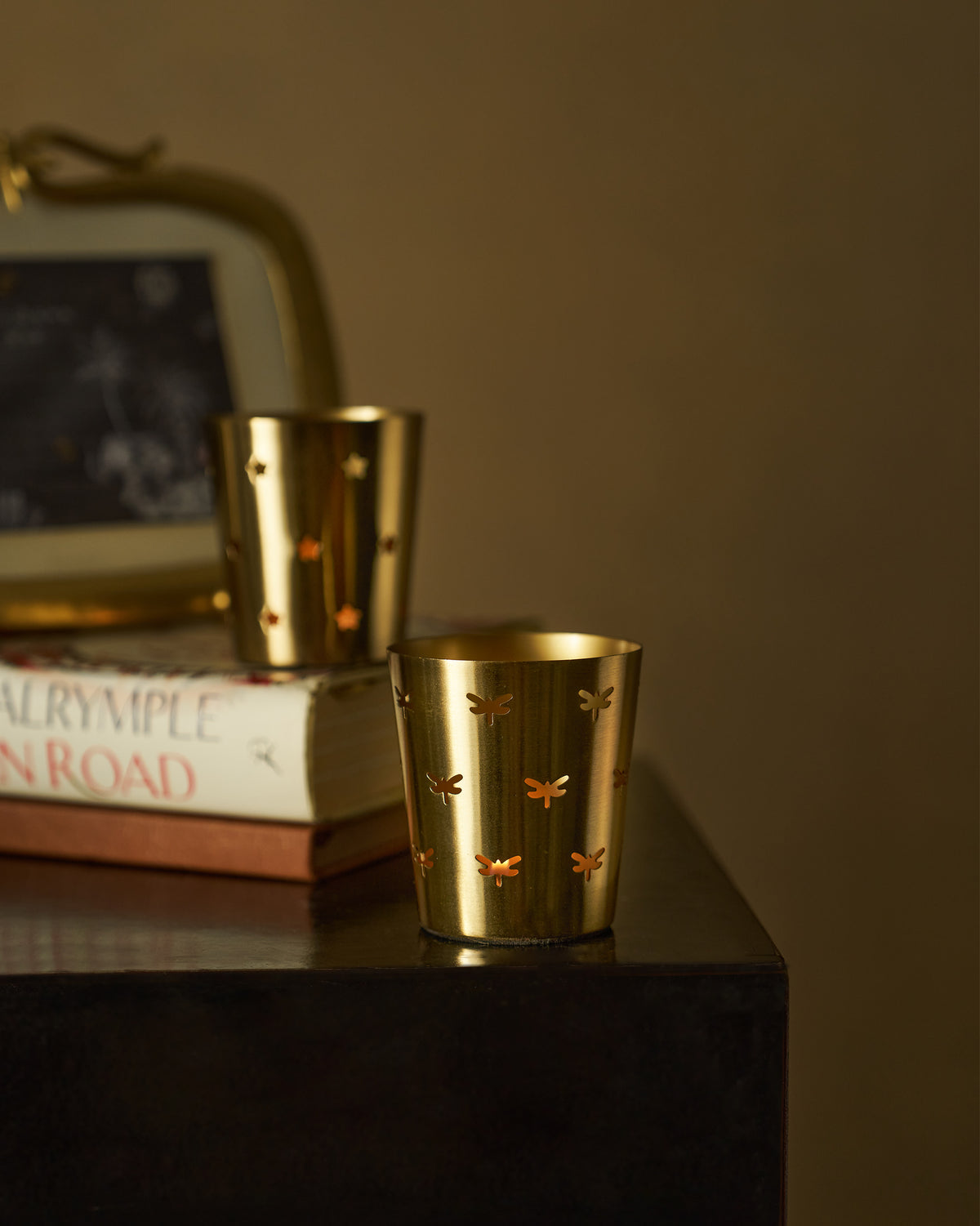 Lit Smriti gold votives with dragonfly and star cutouts glowing through.