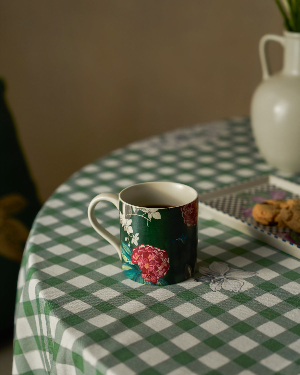 Buransh straight mug of tea on a green gingham tablecloth beside cookies.