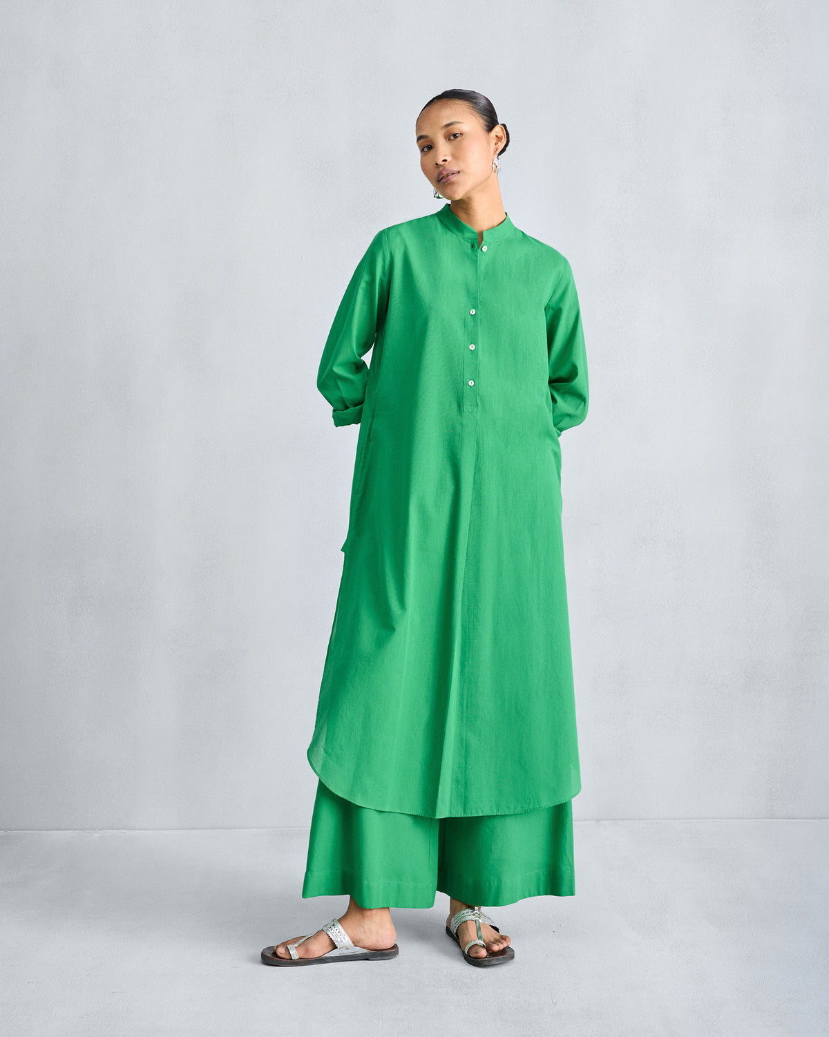 Person wearing a green long kurta with rolled sleeves and matching trousers.