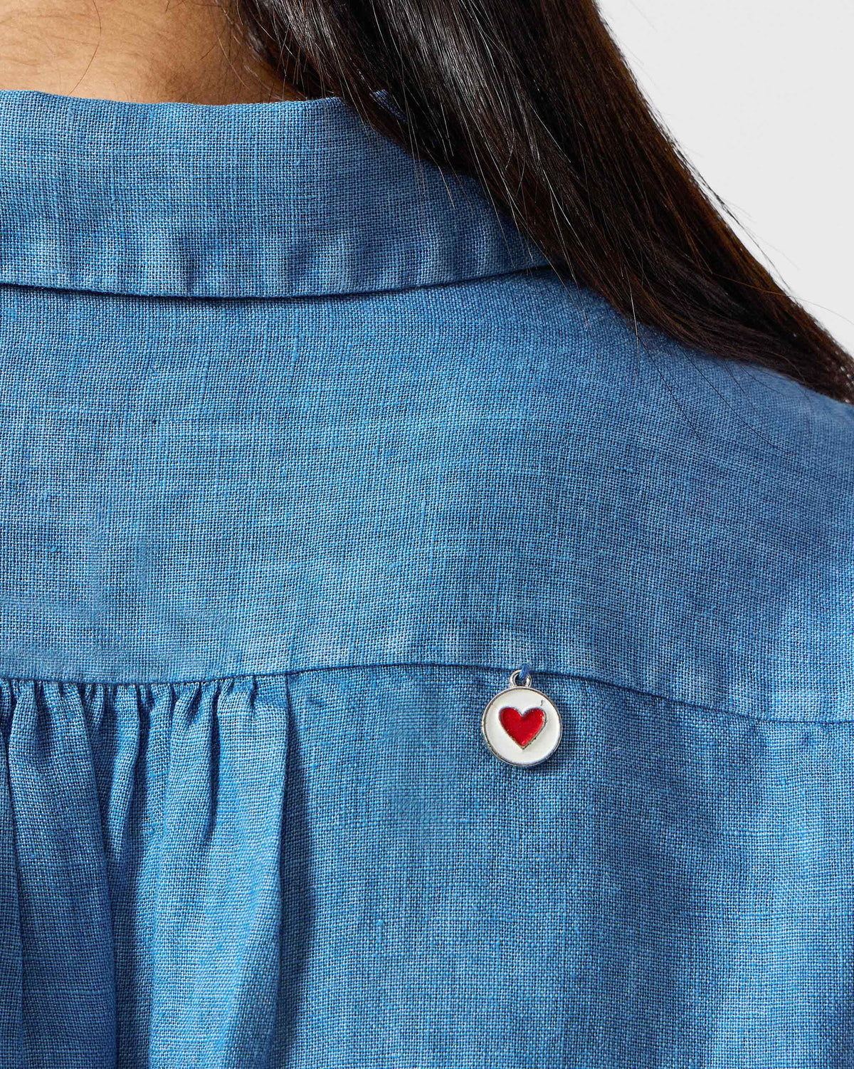 Close-up of a blue Mati shirt showing a red heart charm on the back.