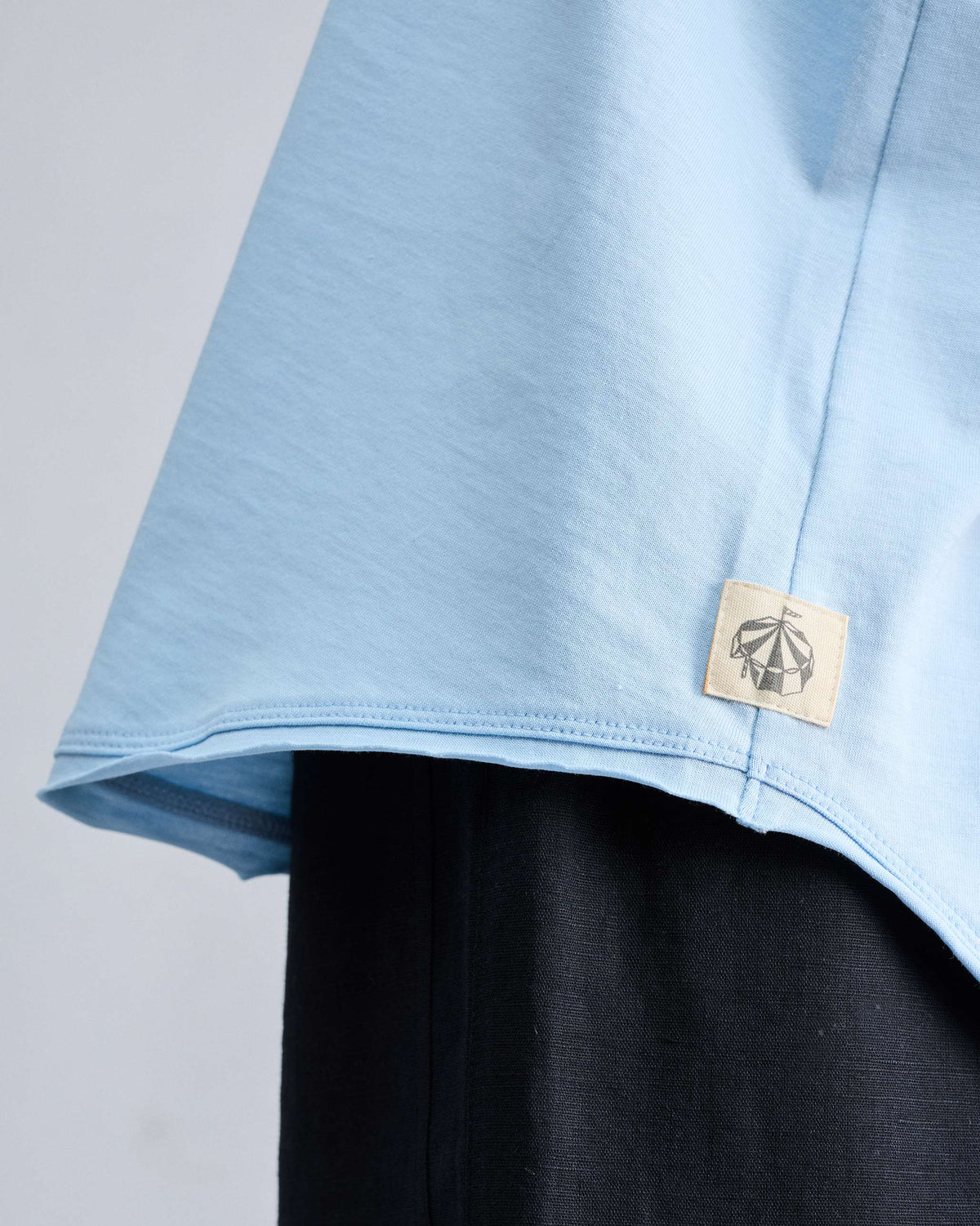 Close-up of a light blue tank hem with a small circus tent patch.