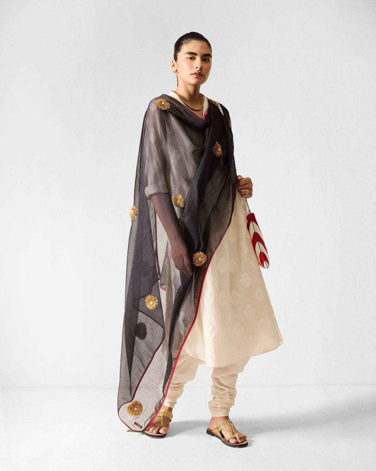 Person wearing an ivory long kurta set with a black gold-embroidered dupatta.